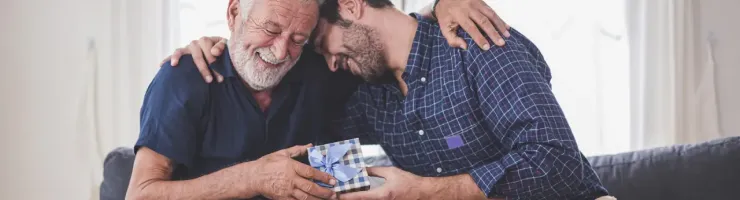 Homme âgé et homme d'âge moyen sont sur le canapé et s'offrent un cadeau.