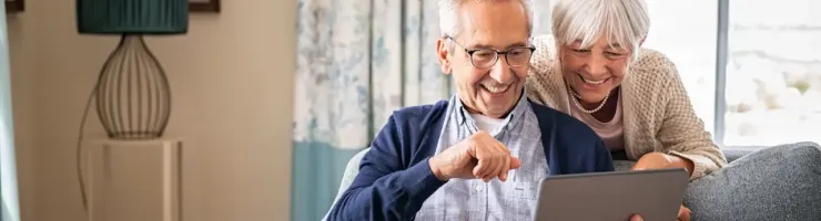 Couple de séniors en train de consulter leur tablette sur leur canapé.
