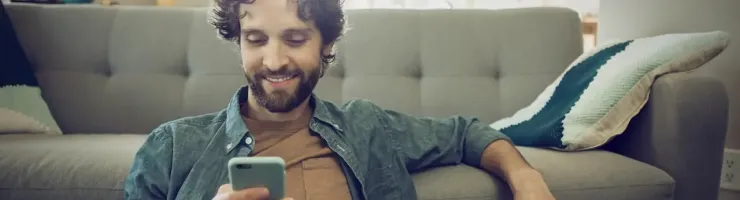 Homme utilise son smartphone devant son canapé.