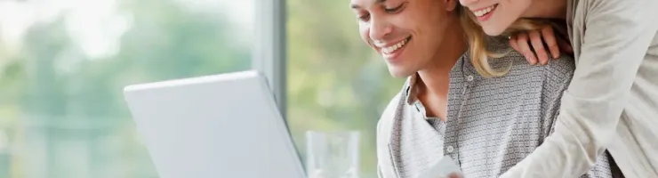 Homme et une femme sourient en regardant un ordinateur sur une table.