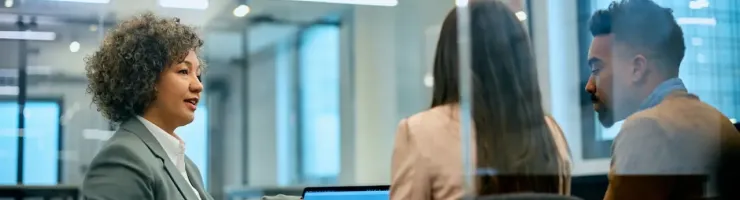 Réunion entre une conseillère bancaire et un couple dans un bureau vitré.