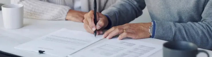 Homme en train de signer des documents en présence de sa femme.