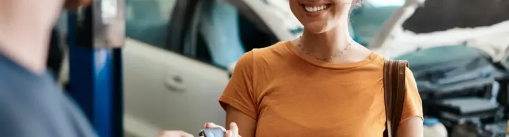 Femme souriante reçoit les clés de sa voiture d'un mécanicien dans un garage.