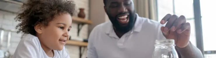 Un papa souriant met une pièce dans un bocal et montre à son fils comment économiser.