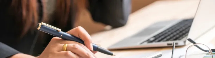 Gros plan d'une main de femme utilise une calculatrice et prend des notes, concentrée sur la gestion de son budget.