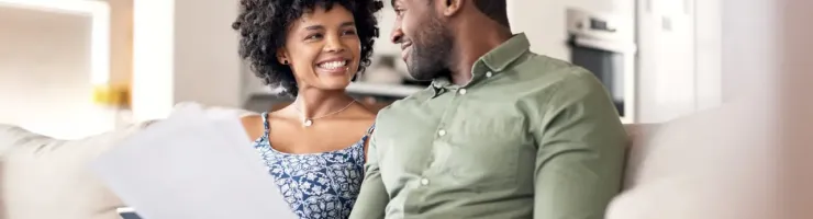 Couple souriant en train tenir des documents et se regarder mutuellement sur leur canapé blanc.