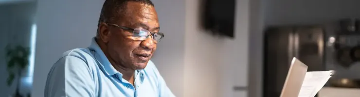 Un homme âgé travaille sur son ordinateur portable dans une pièce sombre et calme.