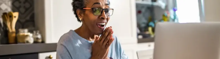 Une femme est assise dans un fauteuil avec un ordinateur portable. Elle est surprise de ce qu'elle vient de voir.