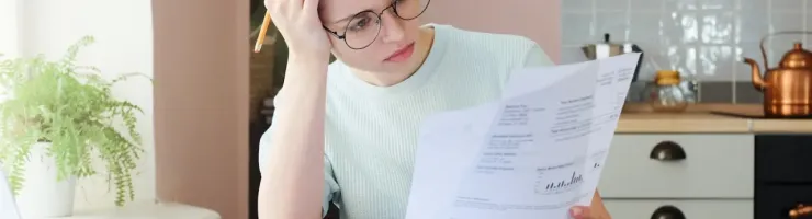 Jeune femme dépassée consulte des documents financiers dans sa cuisine.