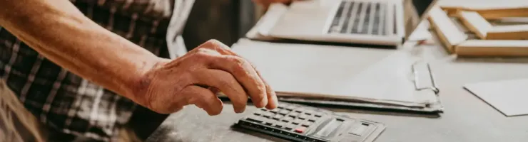 Personne en chemise à carreaux utilise une calculatrice sur un bureau.