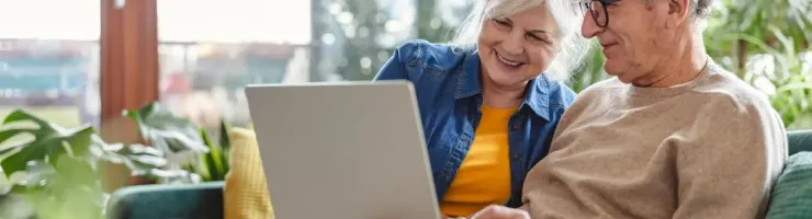 Couple âgé souriant regardant ensemble un ordinateur portable sur un canapé.