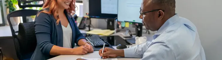 Une femme et un homme discutent autour d'une table dans un bureau moderne et lumineux.