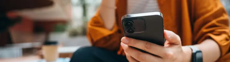 Personne assise, tenant et regardant un téléphone portable.