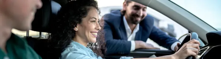 Une femme souriante est au volant d'une voiture. Le commercial de la concession s'appuie sur la fenêtre