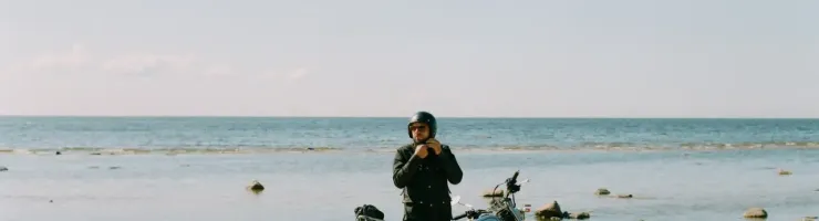 Le motard est en train de mettre un casque de moto sur sa tête. La moto est garée devant la mer