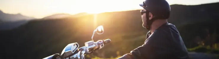 Un homme sur une moto roule au coucher du soleil, casque sur la tête.