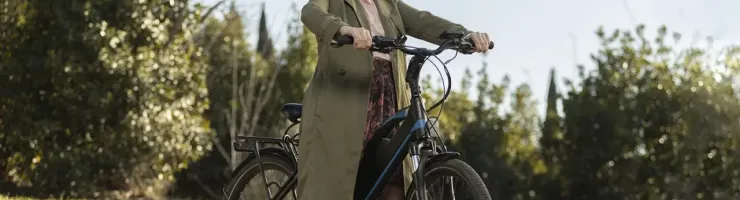 Femme avec casque rose pose avec son vélo sur un chemin ensoleillé.