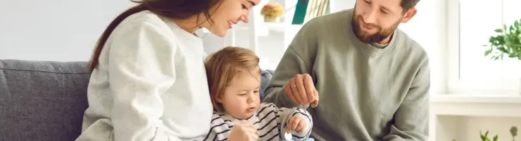 Famille avec enfant est assise sur un canapé et s'apprête à mettre de l'argent dans une tirelire.