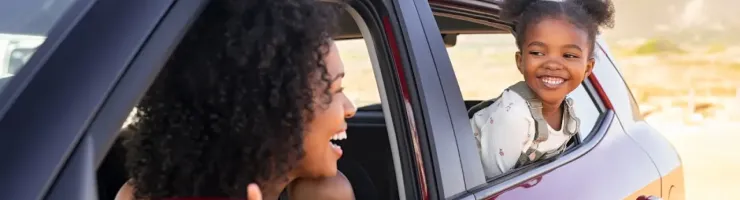 Femme et enfant souriant regardent par les fenêtres d'une voiture rouge.