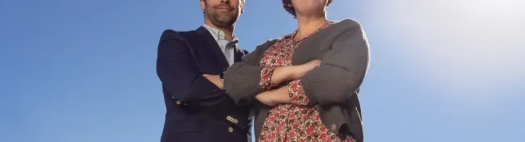 Homme et femme souriants posent avec les bras croisés devant un ciel bleu.