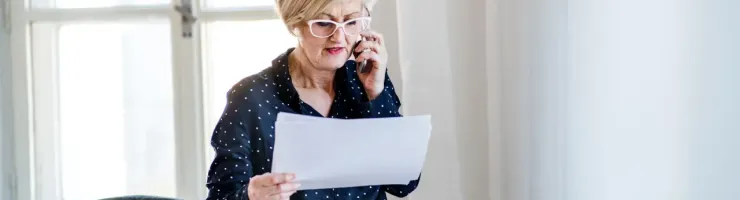 Une femme parle au téléphone et lis des données sur une feuille dans son bureau.