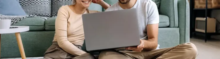 Un couple fait ses comptes en utilisant un ordinateur portable assis par terre.