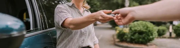 Une femme tend les clés de sa voiture à une autre personne, devant un véhicule stationné.