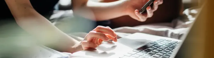 Gros plan montre main qui utilise téléphone et autre utilisant ordinateur.