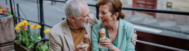 Couple âgé assis sur banc en ville, mangeant des glaces.
