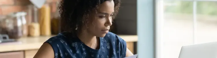 Une femme, tenant un document, utilise son ordinateur portable dans un bureau à domicile.