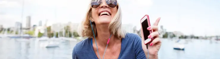 Femme blonde souriante avec lunettes de soleil, écoutant de la musique.