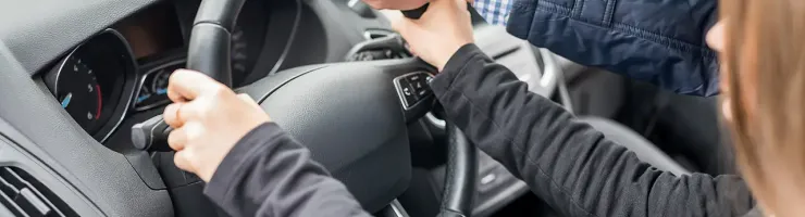 Les mains d'un instructeur guident celles d'un élève sur le volant d'une voiture lors d'une leçon de conduite.