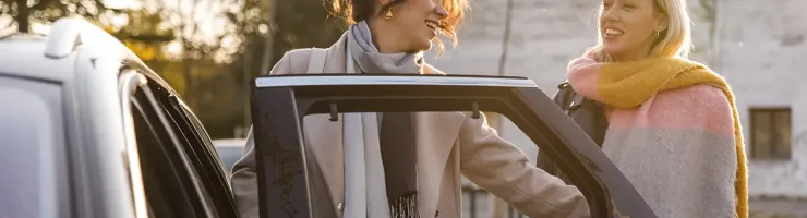 Deux femmes souriantes près d'une voiture, l'une ouvrant la portière.