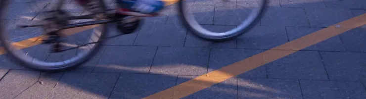 Un cycliste en mouvement sur une piste cyclable pavée avec une ligne jaune, créant un effet de flou dynamique.