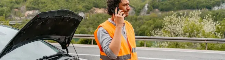 Un homme avec un gilet fluorescent orange est tombé en panne avec son véhicule. Il appelle son assurance pour avoir un dépannage.