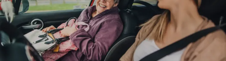 Deux femmes souriantes sont dans un véhicule. La passagère, plus âgée, s'apprête à sortir du véhicule.