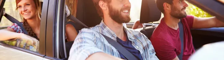 Quatre jeunes amis souriants et joyeux voyagent ensemble en voiture par une journée ensoleillée, profitant de leur trajet.