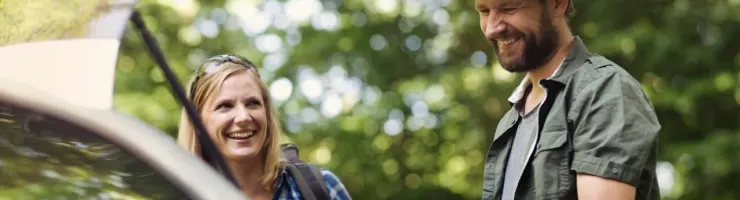 Un couple souriant charge des bagages dans le coffre ouvert d'une voiture.