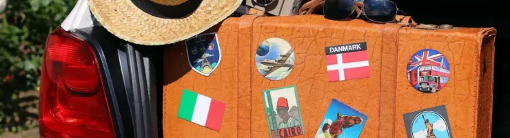 Une valise vintage ornée d'autocollants de voyage est posée à l'arrière d'une voiture, avec un chapeau et une caméra.