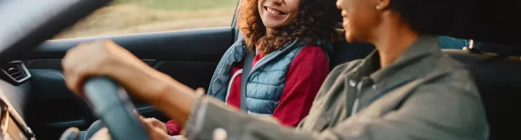 Deux femmes souriantes et heureuses dans une voiture, l'une au volant et l'autre passagère.