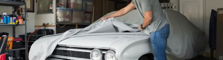 Un homme souriant retire une housse de protection d'une voiture vintage blanche garée dans un garage.