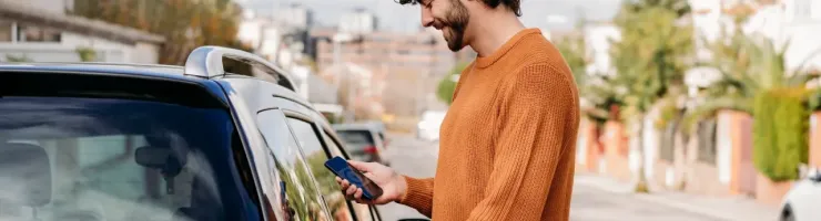 Un homme branche sa voiture électrique chez lui et regarde son téléphone.