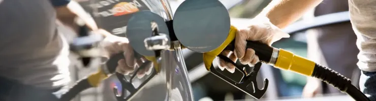 Une main gantée insère un pistolet de pompe à essence dans le réservoir d'une voiture grise, en train de faire le plein.