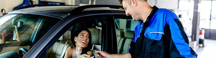 Une femme assise dans une voiture au garage, le garagiste lui donne les clés de son véhicule.