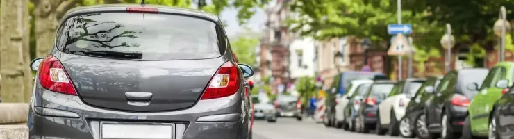 L'arrière d'une voiture grise est garé en épi sur le bord d'une rue bordée d'arbres et d'autres voitures.