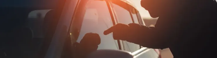 Silhouette d'une personne mal intentionné s'approchant d'une voiture, le soleil couchant créant un fort contre-jour.