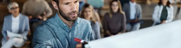 Un expert en sécurité routière écrit sur un tableau, tandis que ses stagiaires l'écoutent attentivement.