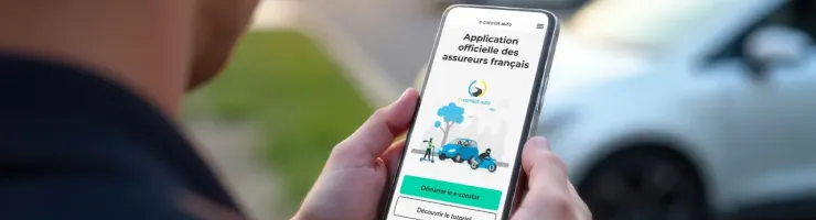 Un homme regarde son téléphone affichant l'application e-constat, sa voiture en arrière-plan.