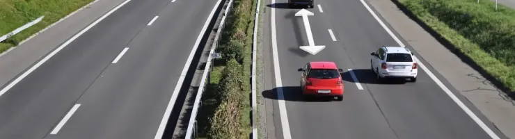 Une autoroute ensoleillée avec plusieurs voitures circulant, des flèches blanches indiquant la distance de sécurité.