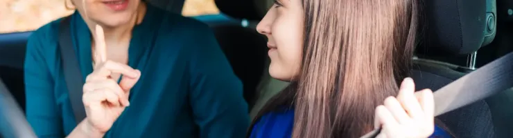 Une mère et sa fille dans une voiture, la mère offrant des conseils à sa fille qui apprend à conduire.